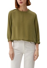 Olivgrünes Longsleeve-Bluse mit rundem Halsausschnitt, gerafften Ärmelbündchen und lockerer Passform. Getragen mit hellen Jeans.