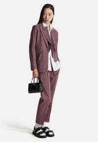 Lila geruite pak met een op maat gemaakt jasje over een witte blouse. Zwarte handtas en zwarte sandalen met witte sokken. Soepele textuur, gestructureerde pasvorm.