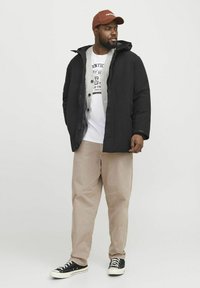 Zwarte pufferjack, grijze hoodie eronder, witte graphic T-shirt, lichtbeige broek, zwarte sneakers met witte zolen, bruine baseballpet.