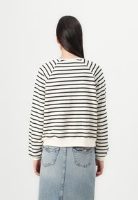 Hvit hettegenser med svarte horisontale striper, med raglanermer og ribbestrikket kant. Brukt sammen med en lys blå denimskjørt.