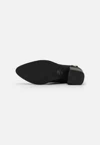Schwarzer High Heel mit spitzem Zehenbereich, strukturiertem Obermaterial und einem klobigen Absatz. Verfügt über eine glatte, flache Gummisohle mit eingeprägtem Branding.
