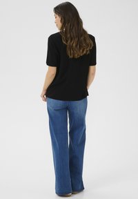 Svart kortärmad topp med avslappnad passform, parat med ljusblå vida jeans av denim. Synliga sömmar och texturerat tyg.
