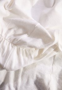 Witte stof met een zachte textuur, voorzien van plooien en geraffineerde details. Het materiaal lijkt lichtgewichtig en licht doorschijnend.