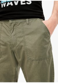 Pantalons légers vert olive avec une finition lisse, présentant des poches latérales et des détails de couture élaborés.