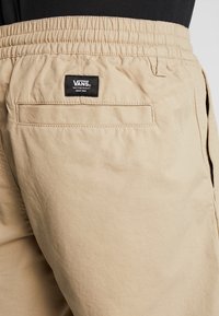 Beige Cargo-Shorts mit elastischem Bund, ausgestattet mit einer Gesäßtasche und einem Vans-Markenlabel, das am Bund aufgenäht ist. Texturiert.