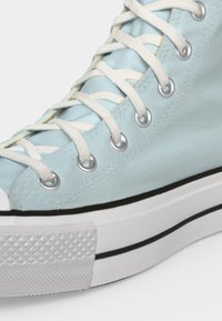 Ανοιχτό μπλε καμβάς sneaker μέχρι τον αστράγαλο με λευκά κορδόνια, ασημένιες τρύπες και χοντρή λευκή καουτσούκ σόλα με μαύρη ρίγα.