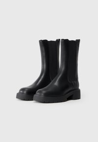 Sorte skinnankelsko med elastiske sidematerialer, runde tær og kraftige gummisåler; glatt tekstur og minimalistisk design.