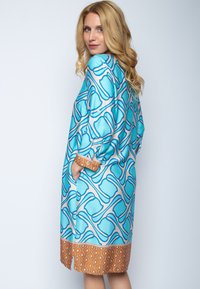Sukienka w niebieskim i beżowym kolorze z geometrycznym wzorem. Posiada długie rękawy, brązowe, wzorzyste mankiety oraz boczne kieszenie.