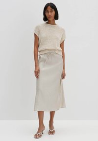 Top in maglia beige a maniche corte abbinato a una gonna leggera beige, lunga fino alla caviglia, con vita elastica e dettaglio con coulisse.