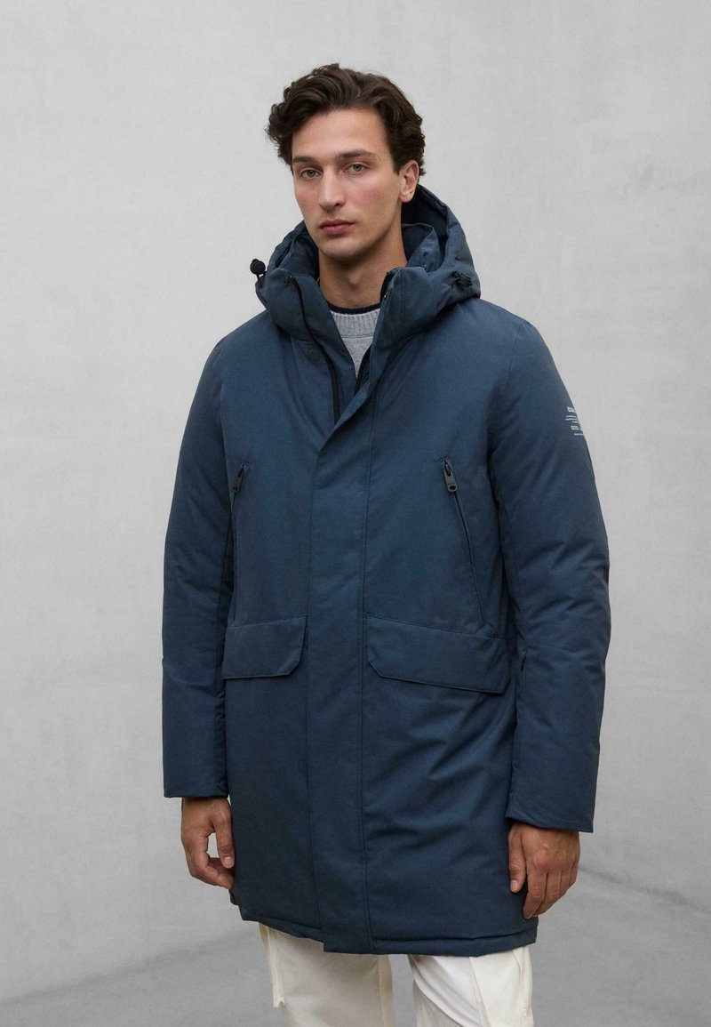 Granatowa kurtka puchowa z kapturem, z dwoma zapinanymi na zamek kieszeniami po bokach oraz zapięciem na guzik. Gładka tekstura, długość do kolan.