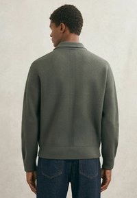 Pulover verde din amestec de lână, cu o croială lejeră, având guler și manșete tivite. Spatele are detalii cu cusături verticale. Poartă-l cu blugi închiși la culoare.