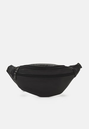 Sac banane en cuir noir avec deux compartiments zippés sur un fond uni gris clair.