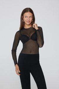 Černý síťovaný top s dlouhým rukávem a puntíky, s přiléhavým st řihem, vrstvený přes černou podprsenku, kombinovaný s černými kalhotami s vysokým pasem.