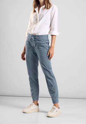 Pantaloni azzurri a sigaretta con vita elasticizzata e coulisse. Dotati di tasche laterali e tessuto liscio e pulito. Abbinati a scarpe da ginnastica bianche.