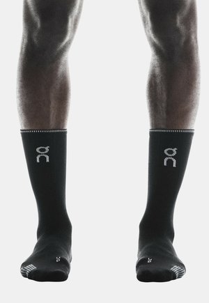 Chaussettes de sport noires avec un bord côtelé, logo à l'avant et orteil renforcé. Présentent une texture lisse et un design au niveau de la cheville.