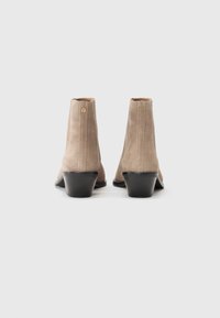 Stivali alla caviglia in suede beige con tacco alto, dotati di cerniera posteriore e design elegante. Superficie strutturata con dettagli minimi.