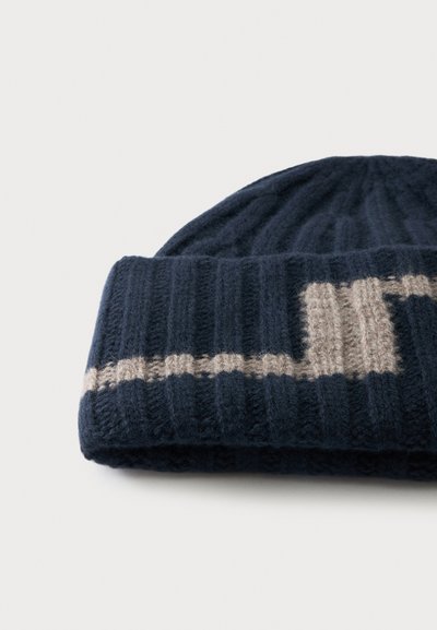 Bonnet en maille côtelée bleu foncé avec un motif zigzag beige sur le bord replié, présenté sur un fond clair uni.