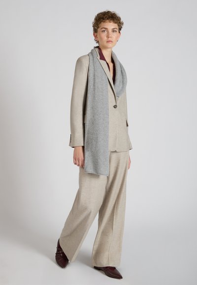 Beige maatpak met wijde broek en een jasje met een sjaalkraag, gecombineerd met een lichtgrijze sjaal en bordeauxkleurige schoenen, gestructureerde stof.