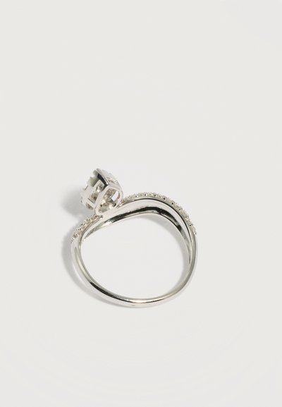 Ασημένιο δαχτυλίδι με μια μικρή ανυψωμένη τετράγωνη βάση και καμπύλη ζώνη μερικώς στολισμένη με μικρές διάφανες πέτρες.