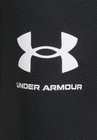 Sort atletisk stof med et hvidt Under Armour-logo. Teksturen er glat med subtile lodrette linjer. Skrifttypen er fed og klar.