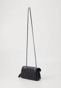 Svart vadderad läderaxelväska med silverkedja och små silvernitar på klaffen, stående mot en enkel ljus bakgrund.