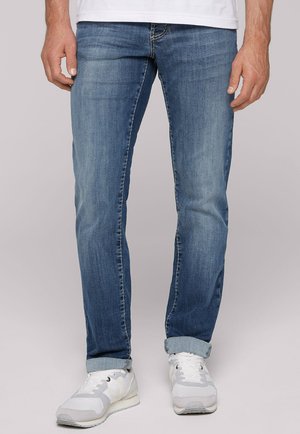 Blaue Jeans im Slim-Fit, mit leichter Ausbleichung und Kontrastnähten, hochgerollten Säumen, kombiniert mit weißen Sportschuhen.