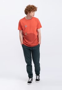 Rode T-shirt met korte mouwen met twee grafische prints, gecombineerd met donkergroene joggingbroek en zwarte sneakers, met elastische boorden en zakken.