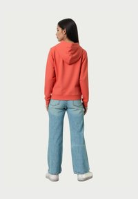 Felpa con cappuccio corallo dotata di tasca a canguro, abbinata a jeans a gamba larga azzurri e scarpe bianche. Tessuto morbido e casual, con una vestibilità rilassata.