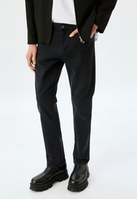 Pantalones de mezclilla negros de corte recto, con cierre de botón y bolsillos frontales, combinados con botas negras de tacón ancho.