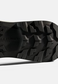 Semelle de chaussure noire robuste avec des crampons profonds pour une meilleure adhérence, présentant le nom de la marque Mammut et le label de design suisse embossés au centre.