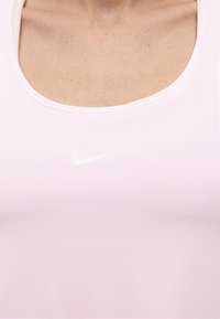 Κοντινό πλάνο ενός ατόμου που φοράει ροζ ανοιχτό μπλουζάκι Nike με λευκό λογότυπο Nike swoosh στο κέντρο του στήθους.