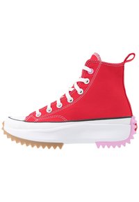 Baskets montantes en toile rouge avec lacets blancs, bout noir, et semelle blanche texturée avec des accents en caoutchouc rose et couleur gomme.