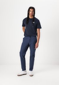 Navy short-sleeve T-shirt with logo, paired with navy drawstring trousers and white sneakers. Casual, relaxed fit with smooth texture.