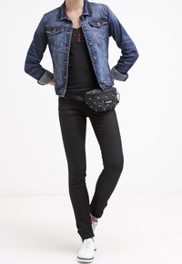 Denimová bunda s běleným efektem, černý tílko, černé skinny jeans a černá ledvinka s bílými puntíky. Bílé tenisky dokončují outfit.