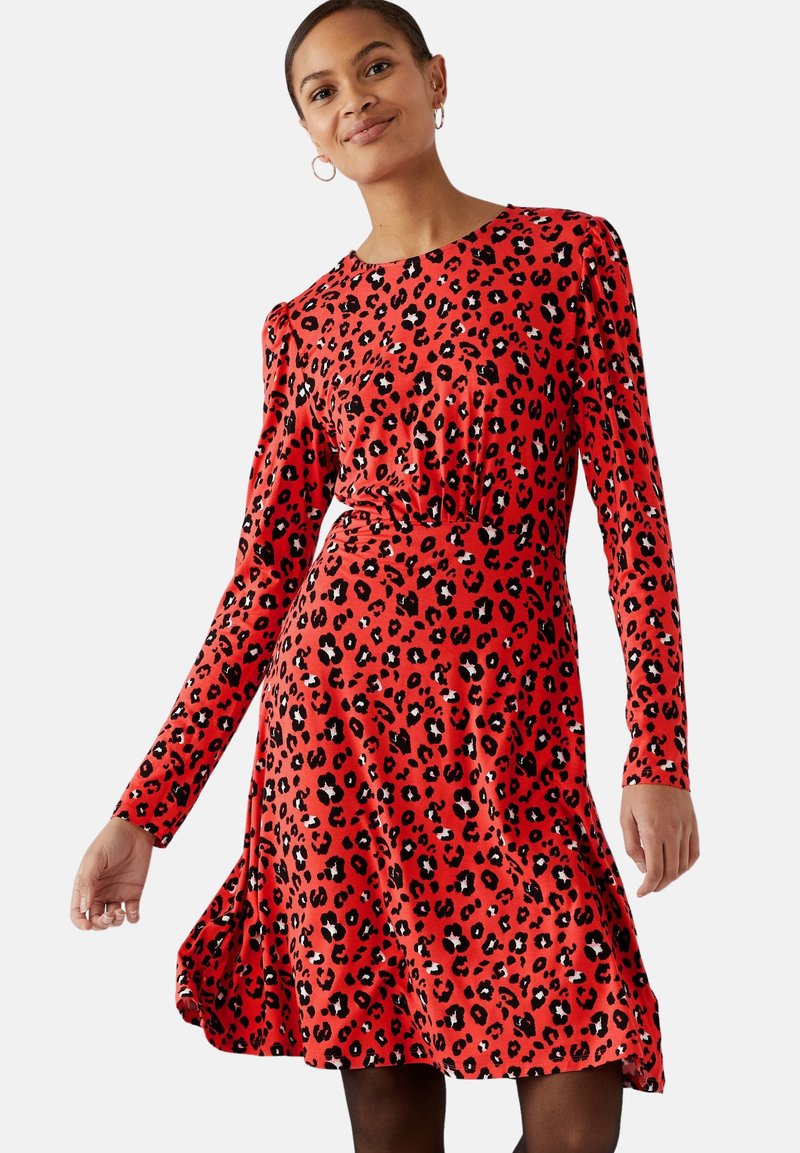 Rotes Langarmkleid mit schwarzem Leopardenmuster, tailliertem Oberteil, lockerer Rock und gerafftem Bund, aus einem glatten, flexiblen Material gefertigt.