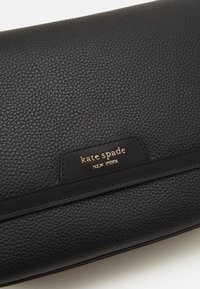 Black leather clutch with a textured finish, featuring a gold logo plate and a smooth band around the body. Compact, rectangular shape.