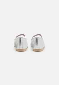 Bailarinas metálicas plateadas con un diseño sencillo, tiras elásticas y una textura suave, con una suela beige plana y un perfil minimalista.