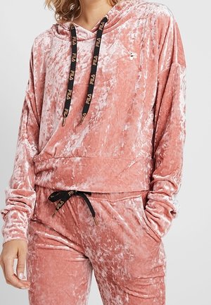 Zachtroze crushed velvet hoodie en bijpassende broekset met zwarte, met merknaam bedrukte trekkoorden en een klein geborduurd logo op de borst.