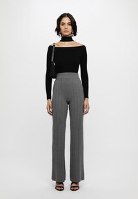 Top negru, cu umerii la vedere, pantaloni gri cu dungi verticale și talie înaltă, sandale plate negre și poșetă mică neagră; design minimalist, ajustat.