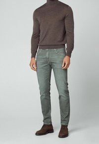 Pull à col roulé marron, jean gris clair coupe ajustée, et chaussures en daim marron. Texture lisse, couleurs neutres, design minimaliste.