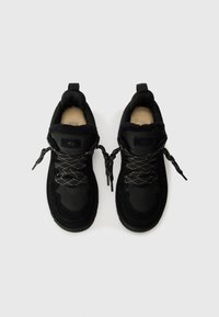 Zwarte sportieve schoenen gemaakt van suede en mesh materiaal, met een gevoerd kraag, patroonnveters en een gestructureerde zool. UGG-logo op de tong.