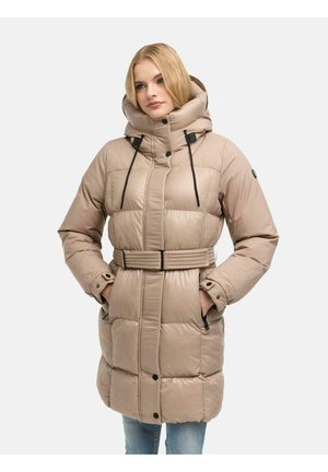 Femme portant un manteau matelassé beige ceinturé, avec un col montant et une capuche, les mains dans les poches, debout devant un fond clair uni.