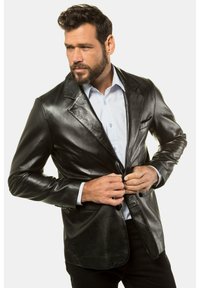 Blazer de cuero negro con solapas de muesca, cierre de un solo botón, dos bolsillos frontales y una textura suave. Llevado sobre una camisa azul clara.