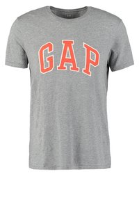 Camiseta de algodón gris con un gran logo rojo de "GAP" en forma de arco en el pecho. Mangas cortas y un diseño clásico de cuello redondo.