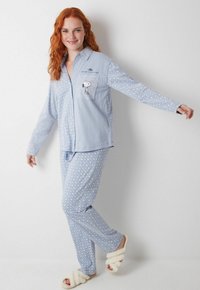 Lyseblåt pyjamassæt med diamantmønster, der har en brystlomme med et Snoopy-tryk. Blødt stof, lange ærmer og behagelig pasform.