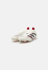 White football boots with black and red accents, textured upper, and molded studs for traction on the field. Sleek, streamlined design.