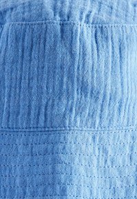 Helle blaue strukturierte Stoff, der gerippte Abschnitte und ein Rautenmuster aufweist. Das Material wirkt weich und atmungsaktiv mit dezenten Steppnähten.