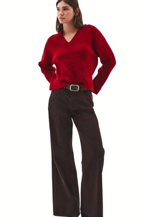 Red knitted v-neck sweater with ribbed texture, paired with high-waisted brown wide-leg pants and a silver buckle belt.
