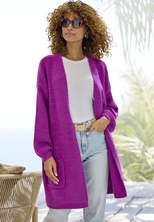 Fuzzy magenta cardigan with open front, long sleeves, and a front pocket, paired with a light shirt and high-waisted denim jeans.