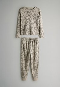 Beige Schlafanzugset mit langärmeligem Oberteil und Hose, das ein Muster aus schwarzen Herzen aufweist. Weicher Stoff, elastischer Bund und gerippte Bündchen.